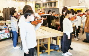 バイオリンの持ち方を練習する小学生と保護者