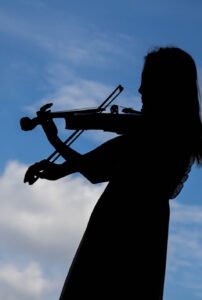 青空を背景にバイオリンを演奏する女性のシルエット