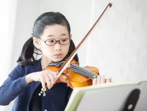 楽譜をみながらバイオリンを練習する小学生