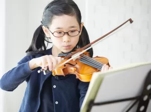 楽譜をみながらバイオリンを練習する小学生