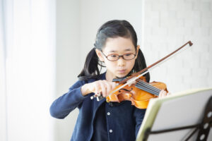 楽譜をみながらバイオリンを練習する小学生