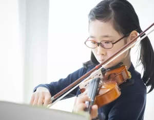 楽譜をみながらバイオリンを練習する小学生