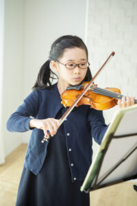 楽譜をみながらバイオリンを練習する小学生