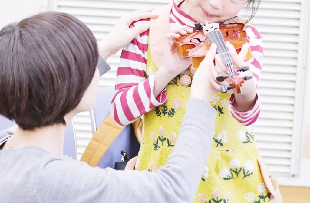 バイオリンを顎で挟もうと頭を倒す子ども（誤った例）